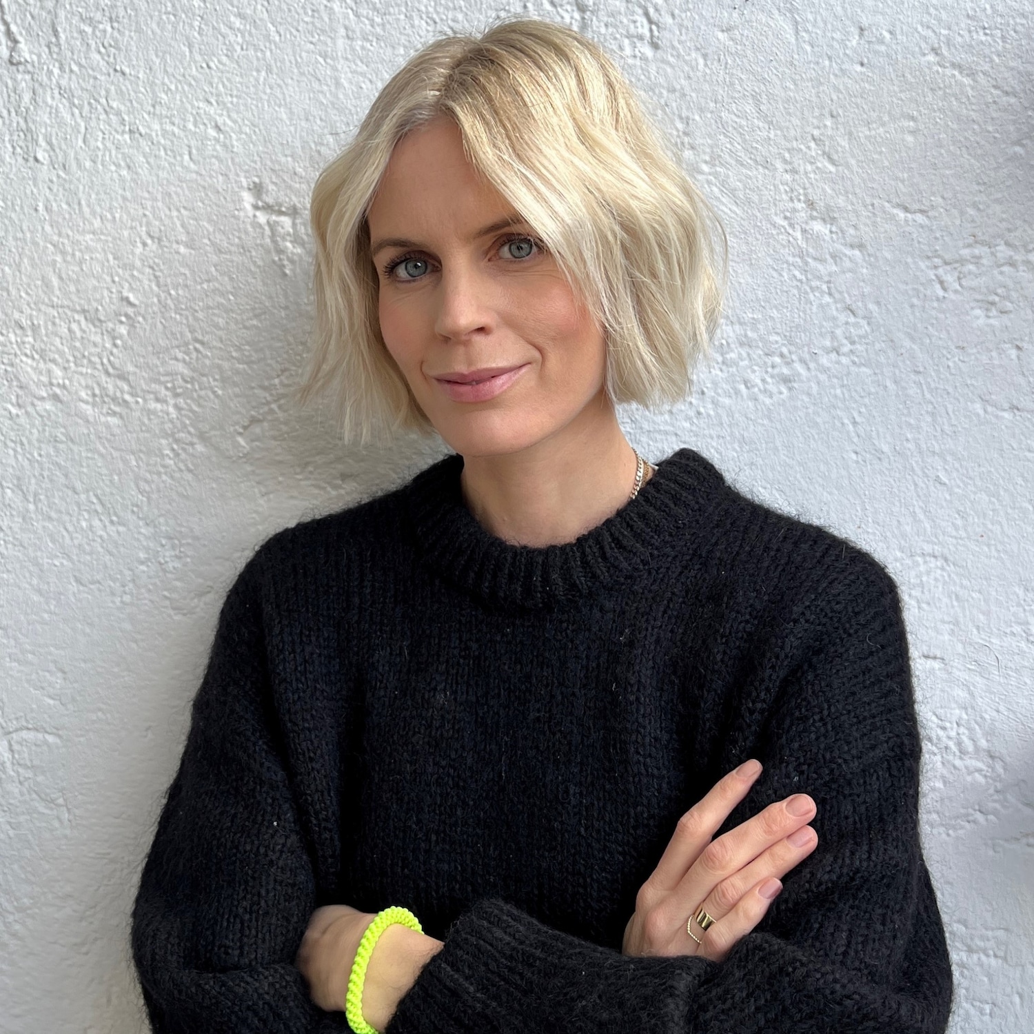 Eine Frau mit blonden, gewellten Haaren und blauen Augen, die einen schwarzen Pullover trägt.