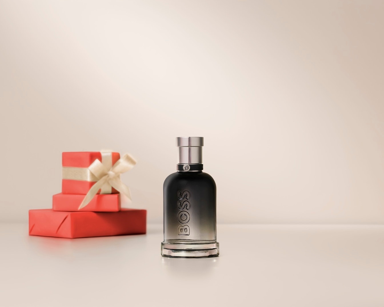 Le parfum BOSS The Scent Elixir est présenté à côté de deux cadeaux emballés dans du papier rouge et décorés d'un ruban beige.
