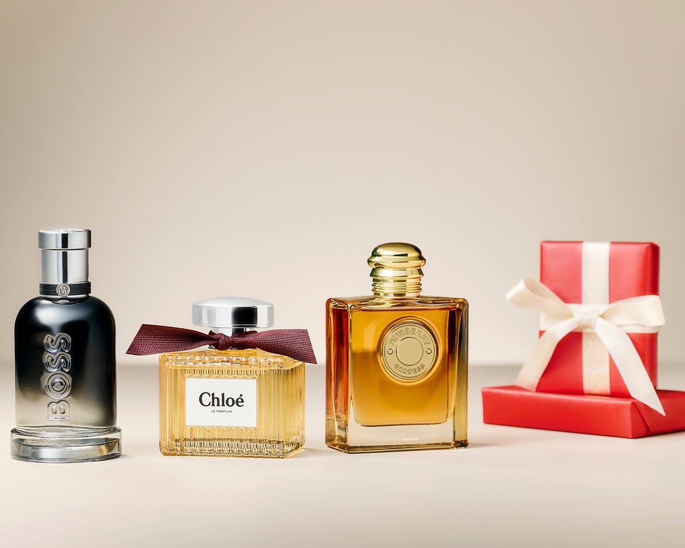 Découvrez un assortiment de parfums de marques renommées telles que Boss, Chloé et Burberry, présentés à côté d'un cadeau emballé, parfaits pour offrir.
