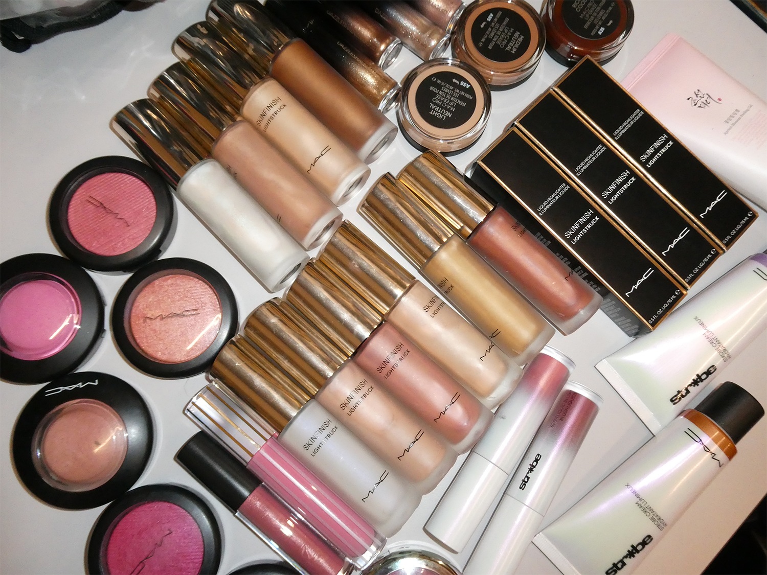 Een verzameling MAC-make-up, waaronder blushers, Skinfinish Lightstruck-highlighters en Strobe Cream Hydratant Lumineux, allemaal in verschillende tinten en texturen.