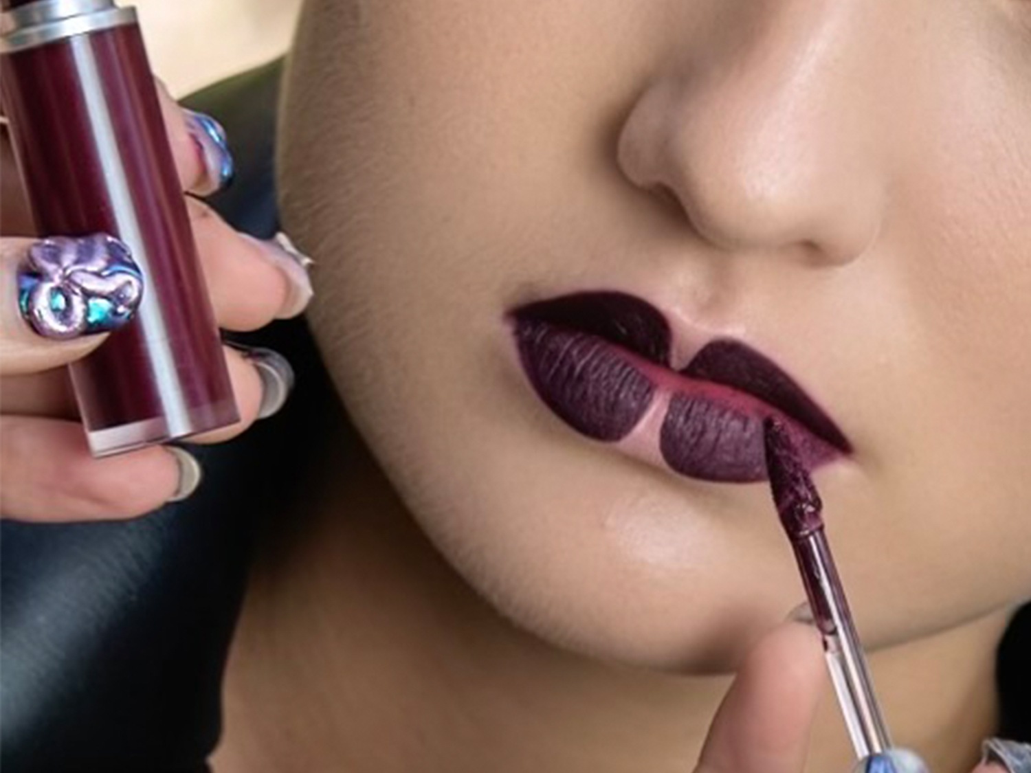Close-up van een vrouw die een dieppaarse vloeibare lippenstift aanbrengt met een applicator, wat zorgt voor een gedurfde en intense kleur.