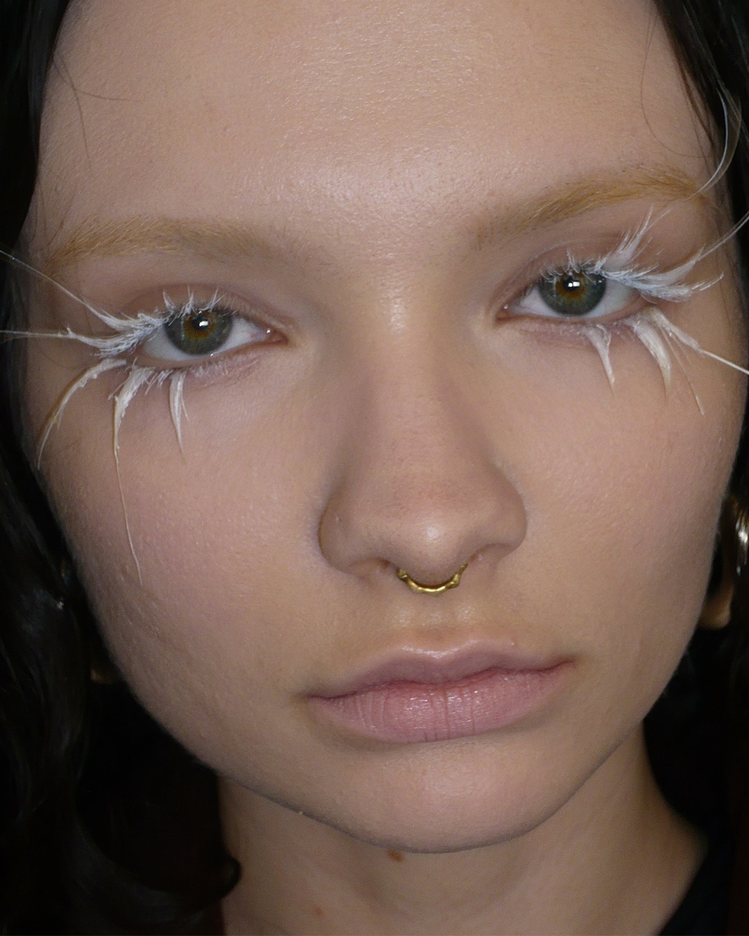 Een close-up van een gezicht met opvallende witte make-up rond de ogen, die een artistieke en avant-gardistische uitstraling creëert.