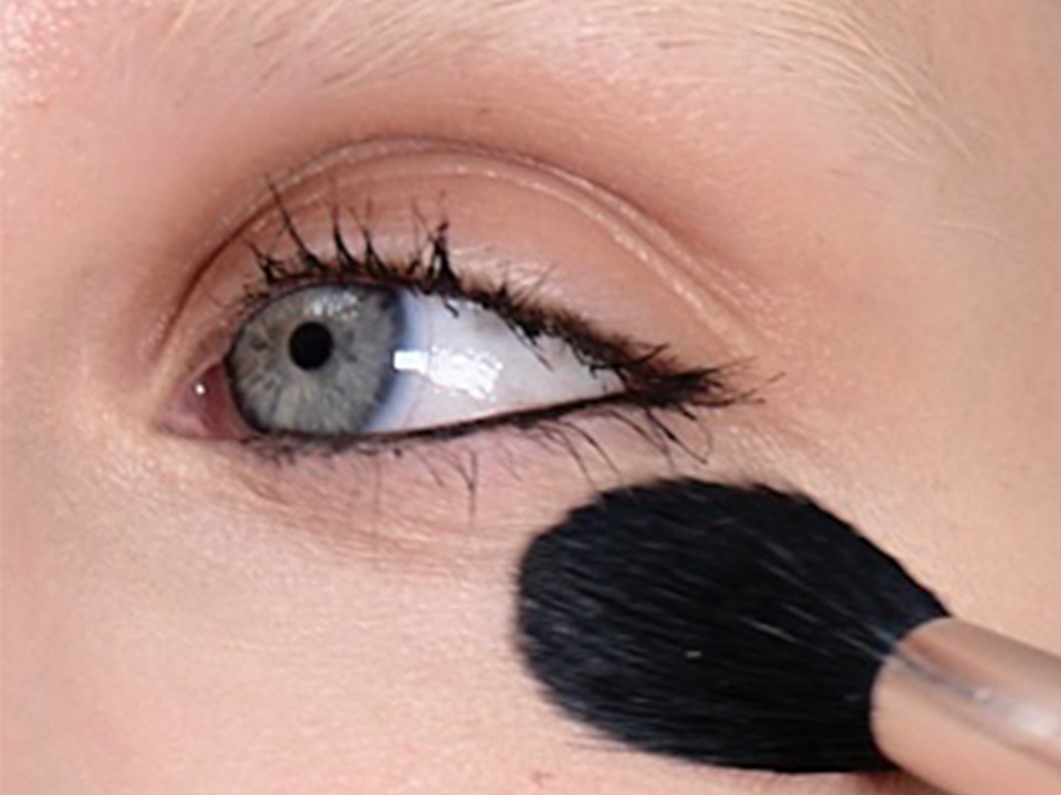 Close-up van een oog met zwarte eyeliner en een make-upborstel die onder het oog wordt gebruikt.
