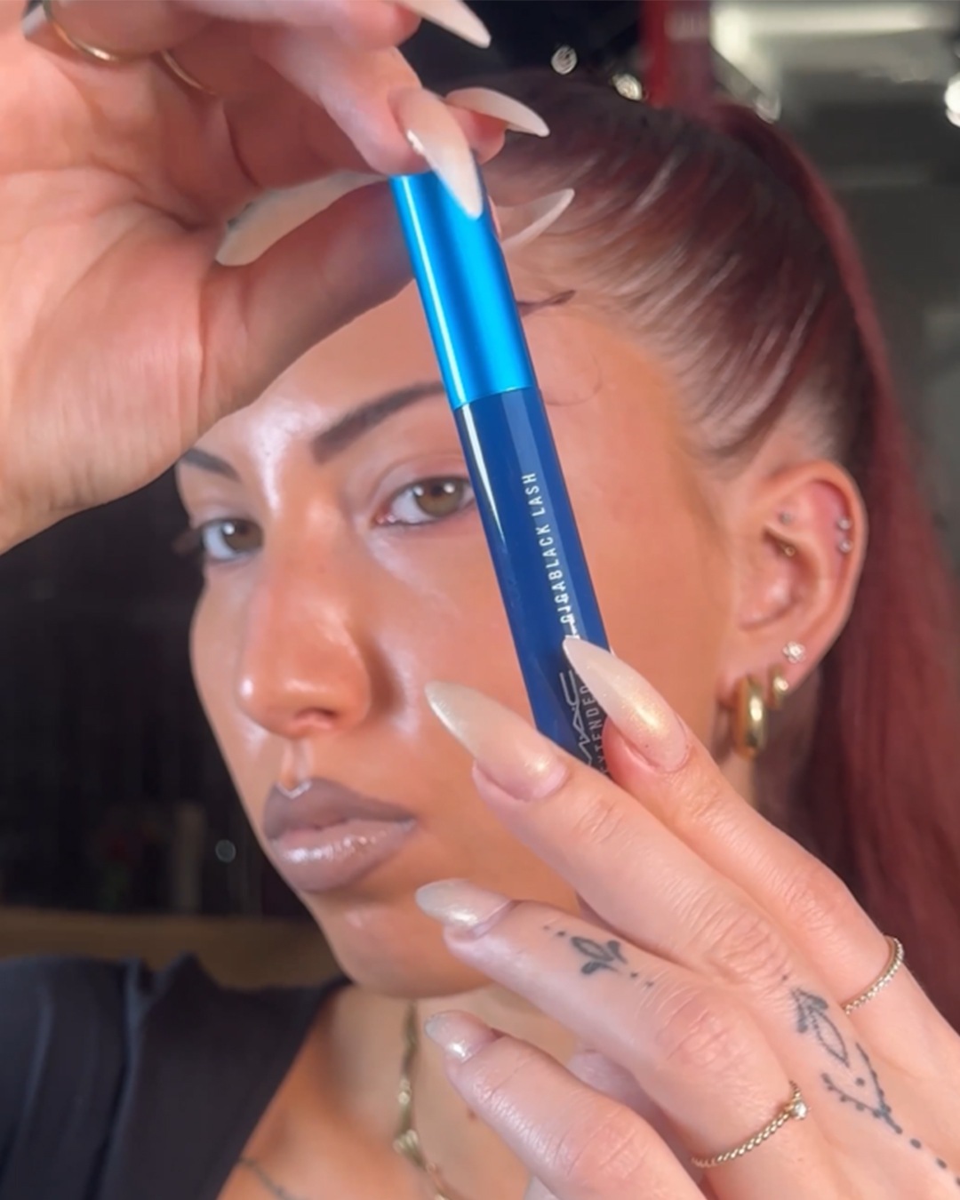 Een vrouw houdt een blauwe MAC Extended Play Gigablack Lash mascara vast, klaar om haar wimpers te accentueren voor een verleidelijke oogopslag.