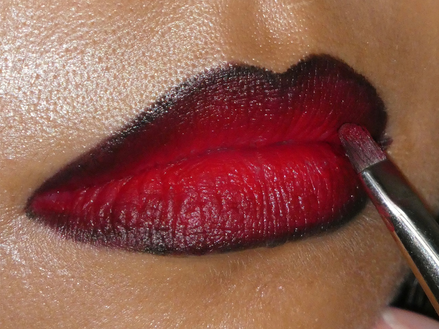 Close-up van lippen met een rode ombre-lippenstift die wordt aangebracht met een penseel, waarbij de kleur overgaat van donker aan de buitenkant naar helder in het midden.
