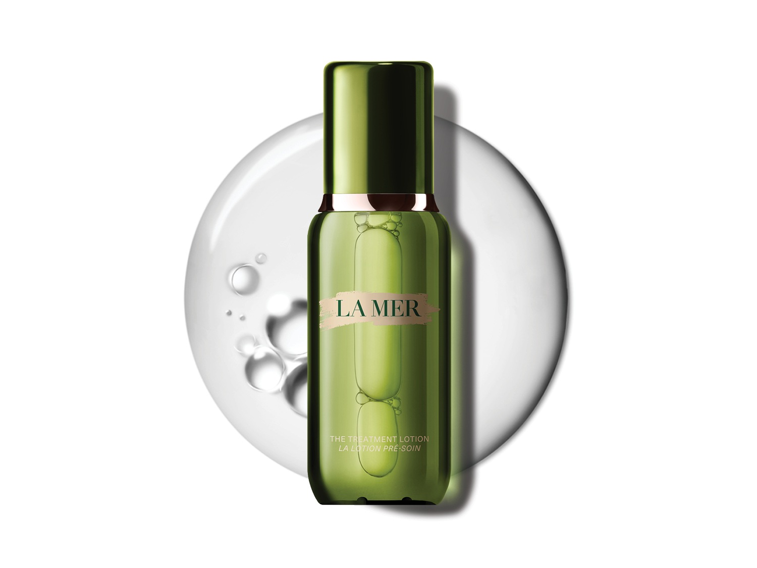 Butelka La Mer The Treatment Lotion w odcieniach zieleni z płynem w środku, otoczona kroplami wody, tworzy wrażenie świeżości i nawilżenia.