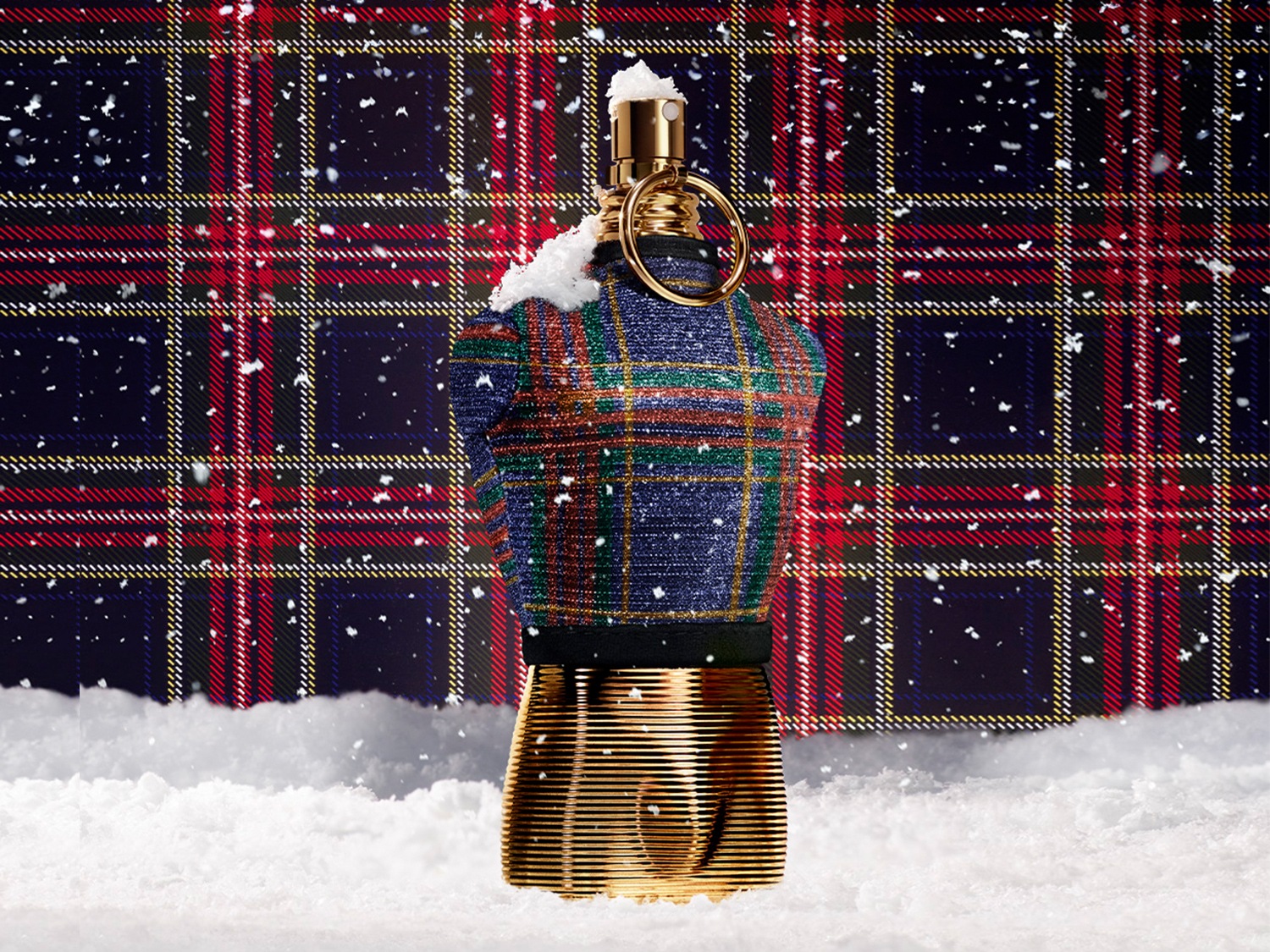 El frasco dorado de perfume Le Male de Jean Paul Gaultier está vestido con un suéter de tartán azul, verde y rojo, perfecto para la temporada navideña.