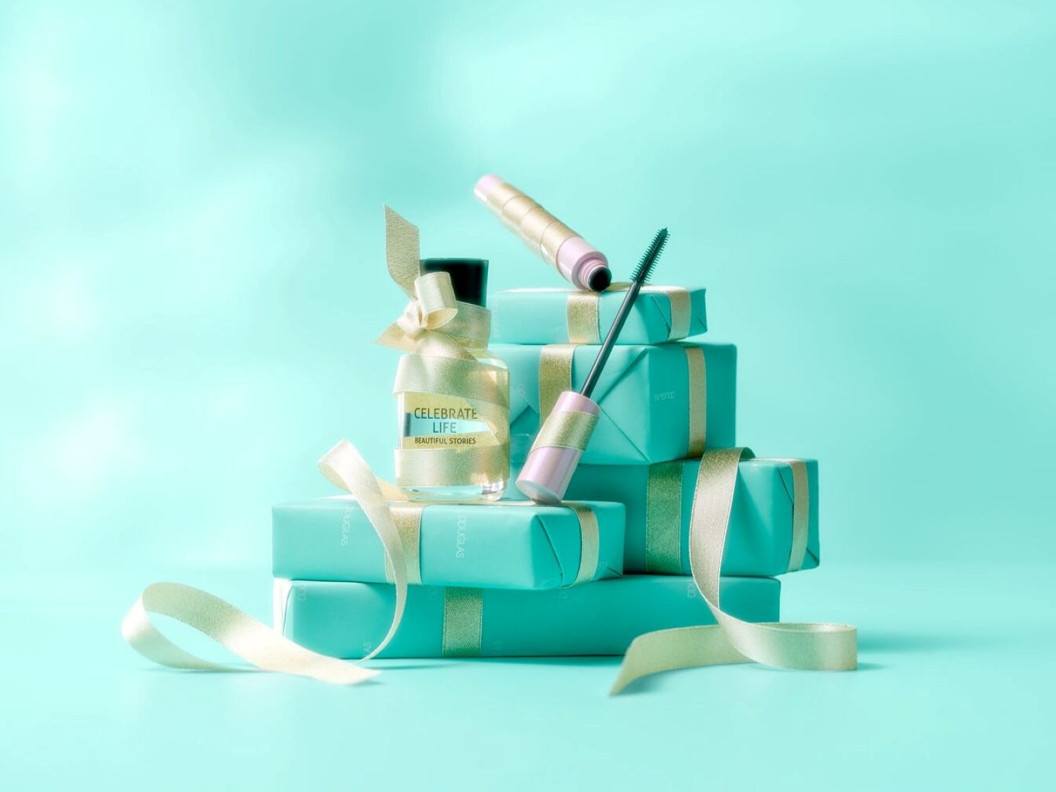 Ecco una pila di regali avvolti in carta turchese e nastro dorato, con un flacone di profumo "Celebrate Life Beautiful Stories" e un mascara rosa e oro in cima.