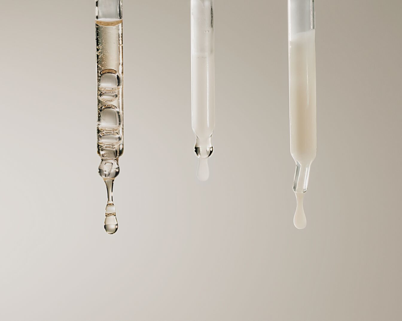 Tre contagocce mostrano sieri di diversa consistenza: uno trasparente e oleoso, uno bianco latte e uno bianco opaco, per illustrare la varietà di prodotti per la cura della pelle.