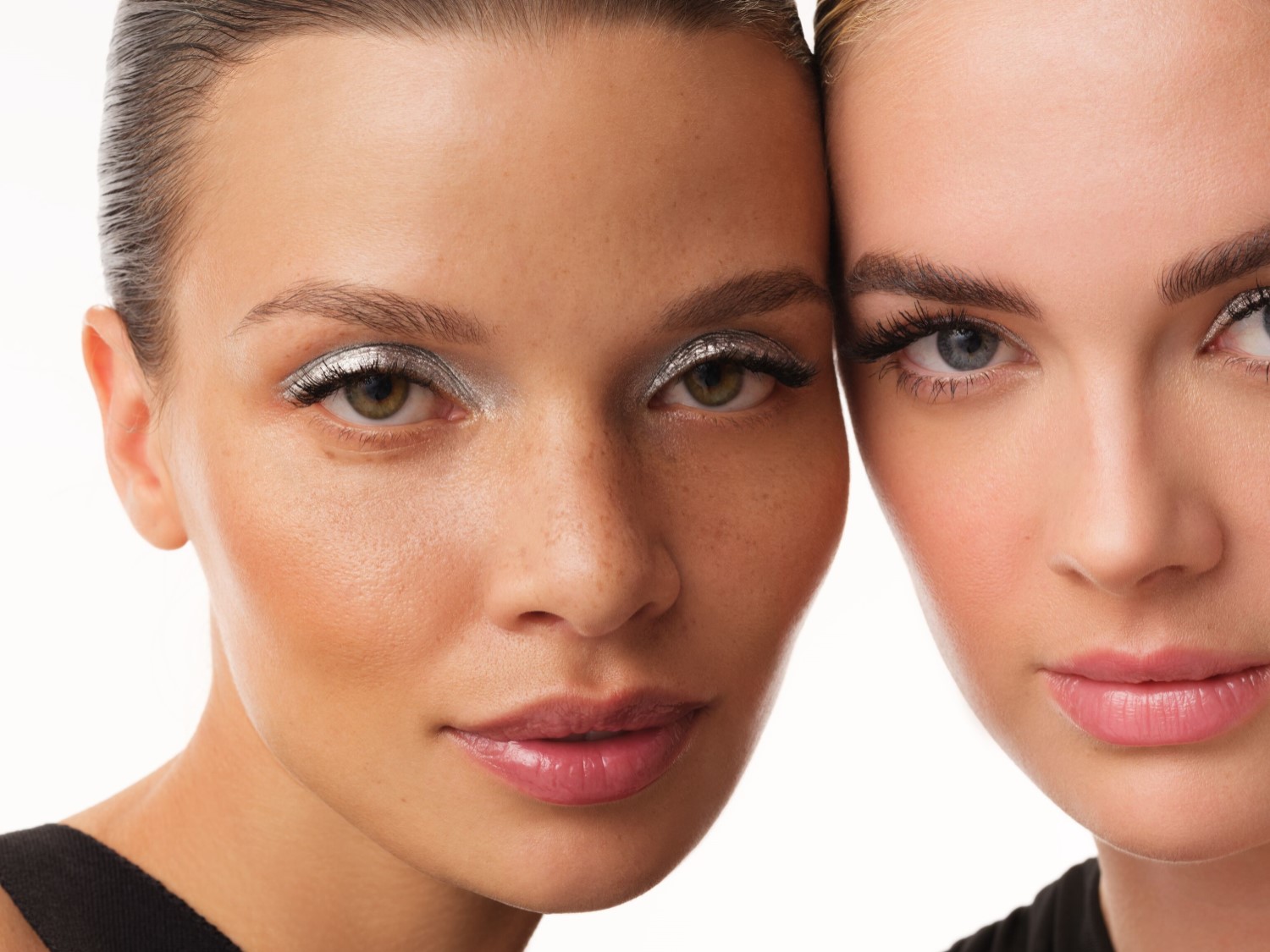Nahaufnahme von zwei Frauen mit silbernem Lidschatten, die ihre Wangen aneinanderlegen und einen strahlenden, glamourösen Look zeigen.