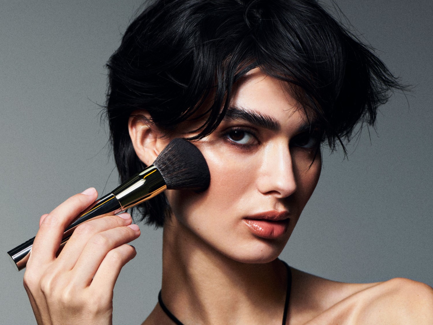 Nahaufnahme einer Person, die mit einem Pinsel Make-up aufträgt, um einen makellosen und strahlenden Teint zu erzielen.