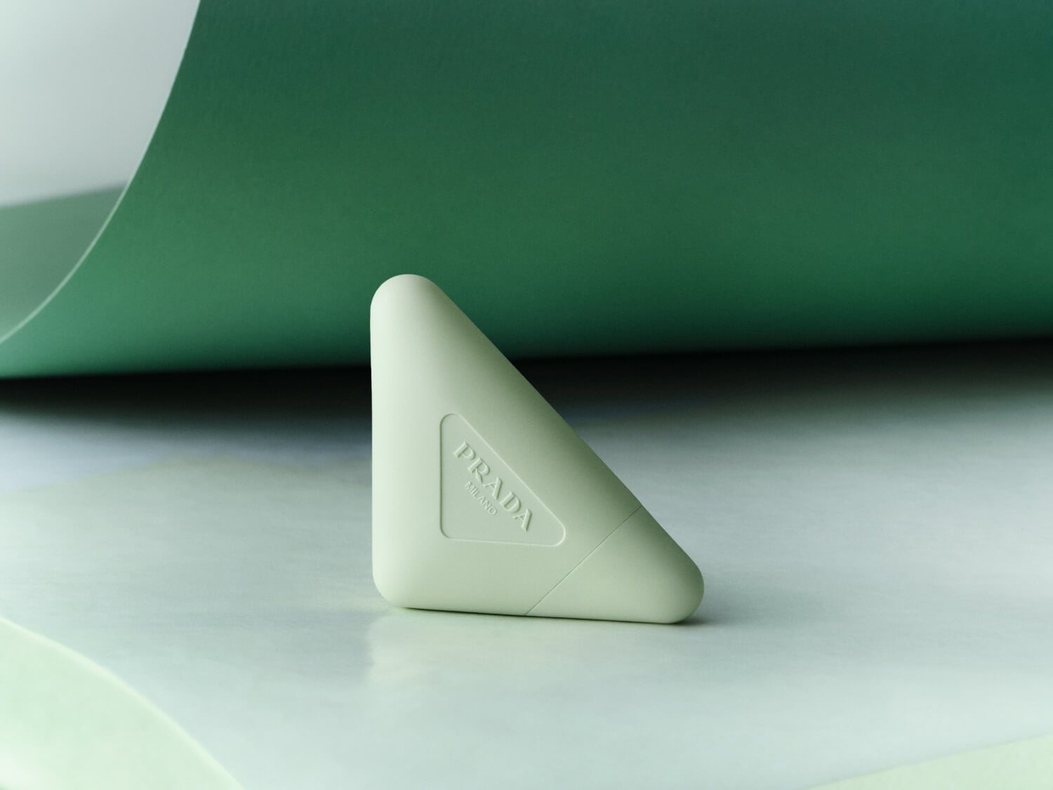 Nahaufnahme eines hellgrünen Prada-Parfümflakons in dreieckiger Form mit abgerundeten Ecken, der auf einer hellgrünen Oberfläche vor einem mintgrünen Hintergrund steht.