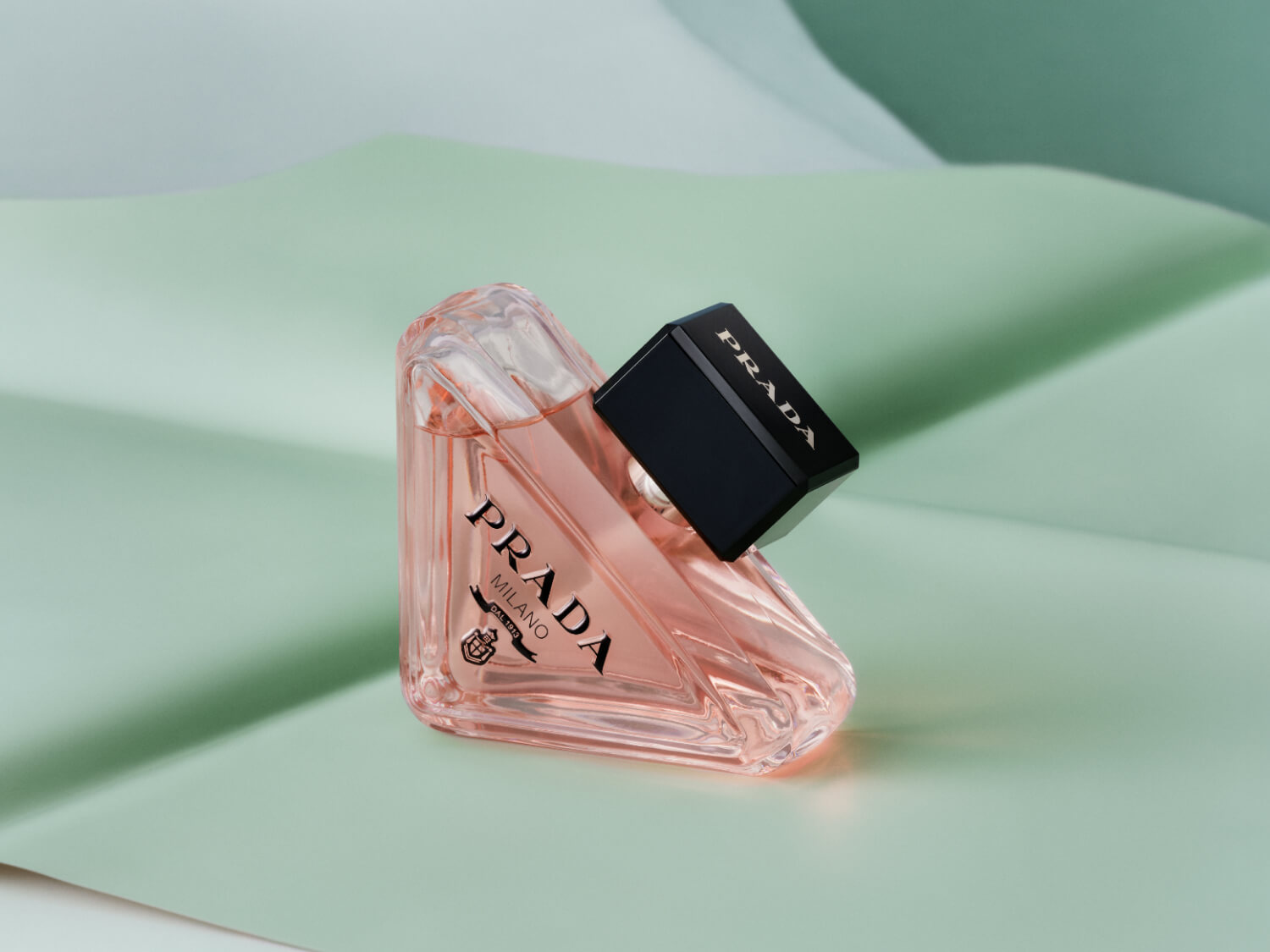 Prada Milano Damenduft in einem transparenten, rosafarbenen Flakon mit schwarzem Verschlusskappe, präsentiert auf einem hellgrünen Hintergrund.