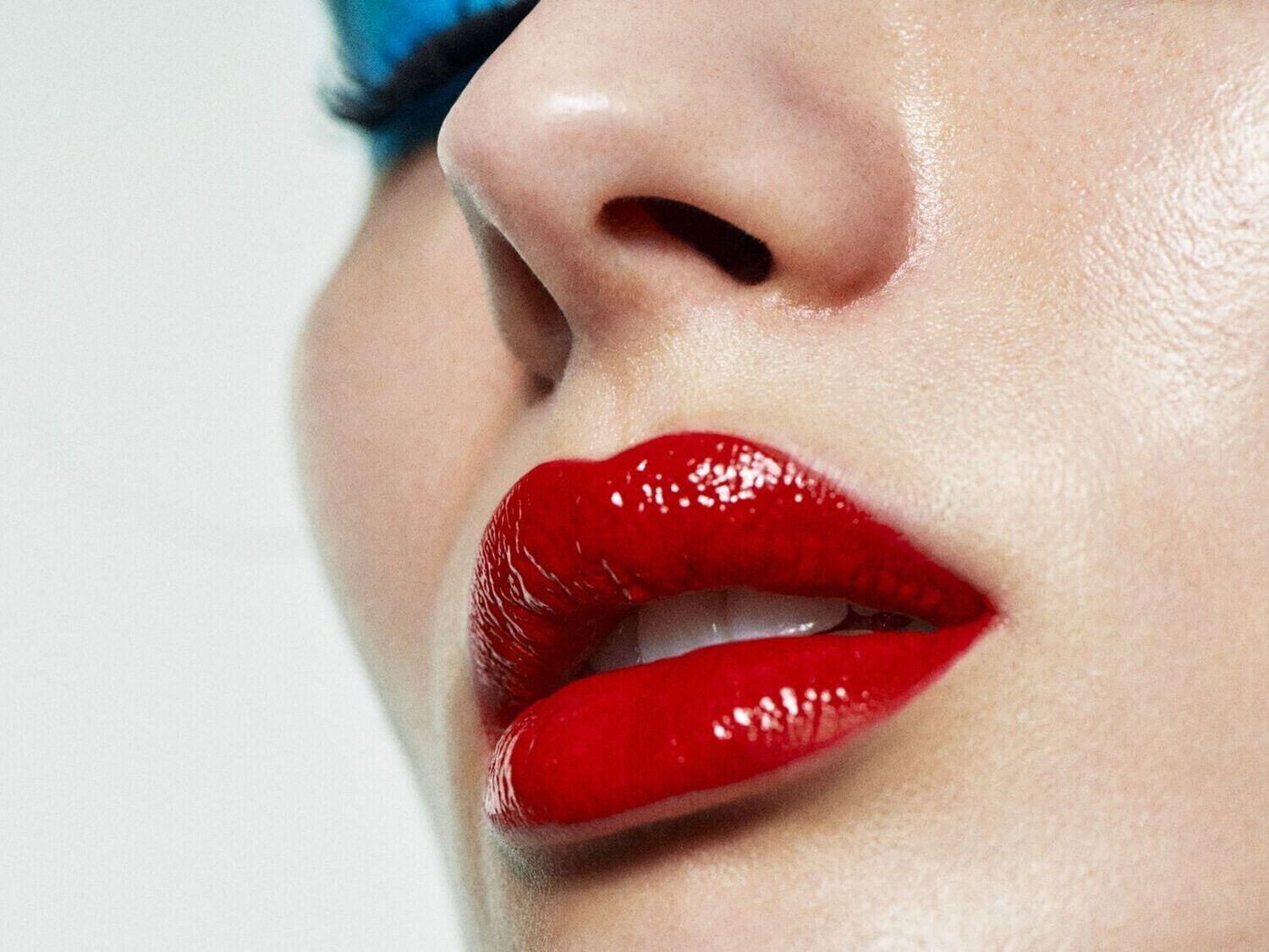 Ryškiai raudoni lūpų dažai ant moters, kurios oda švyti, o mėlyni šešėliai suteikia įvaizdžiui dramatiškumo.