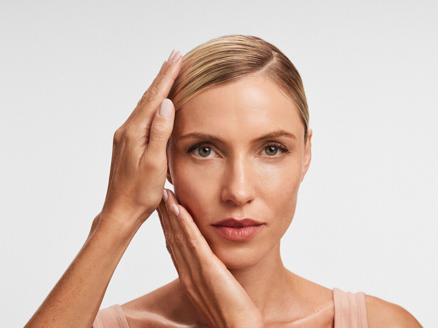 Šviesiaplaukė moteris švelniai liečia savo veidą, pabrėždama odos priežiūros svarbą.