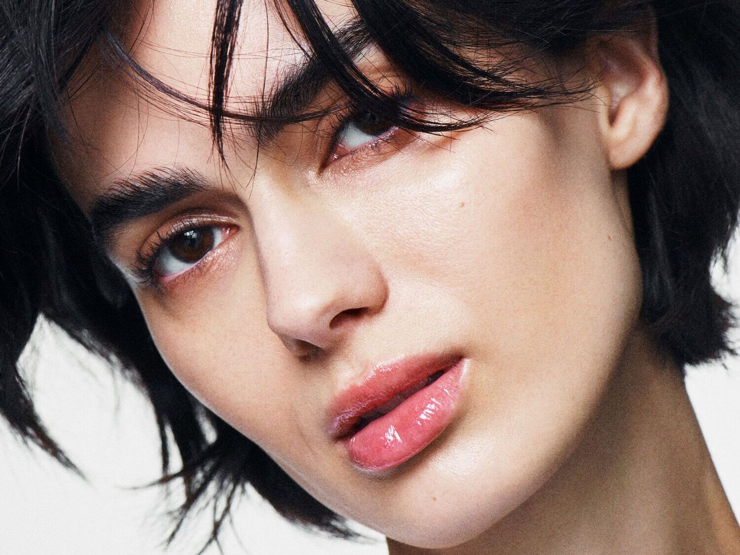 Moters veidas su švytinčiomis lūpomis ir tamsiais plaukais, pabrėžiančiais natūralų grožį.