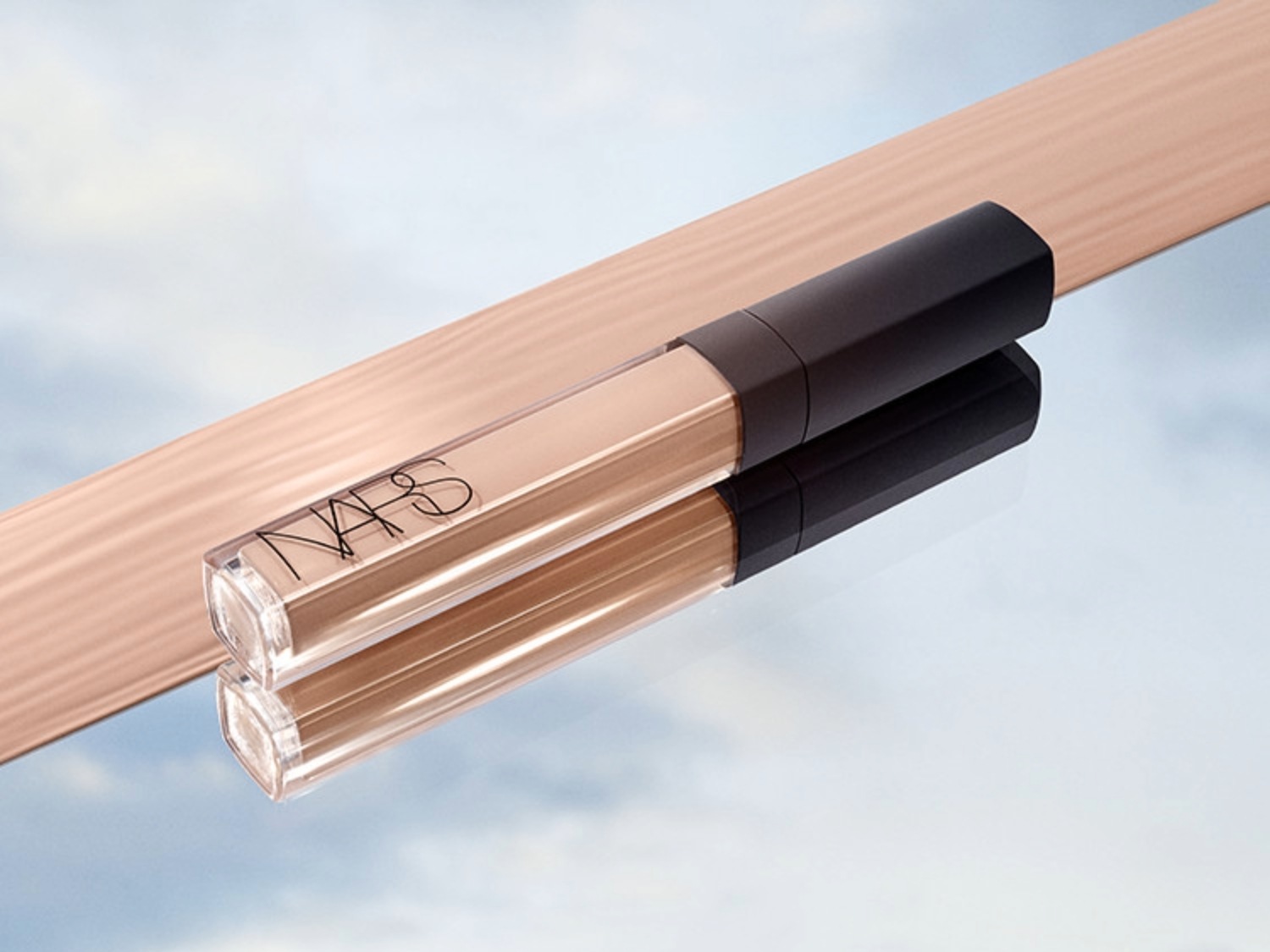 NARS concealer met een heldere, transparante verpakking en een zwarte dop, liggend op een spiegelend oppervlak.