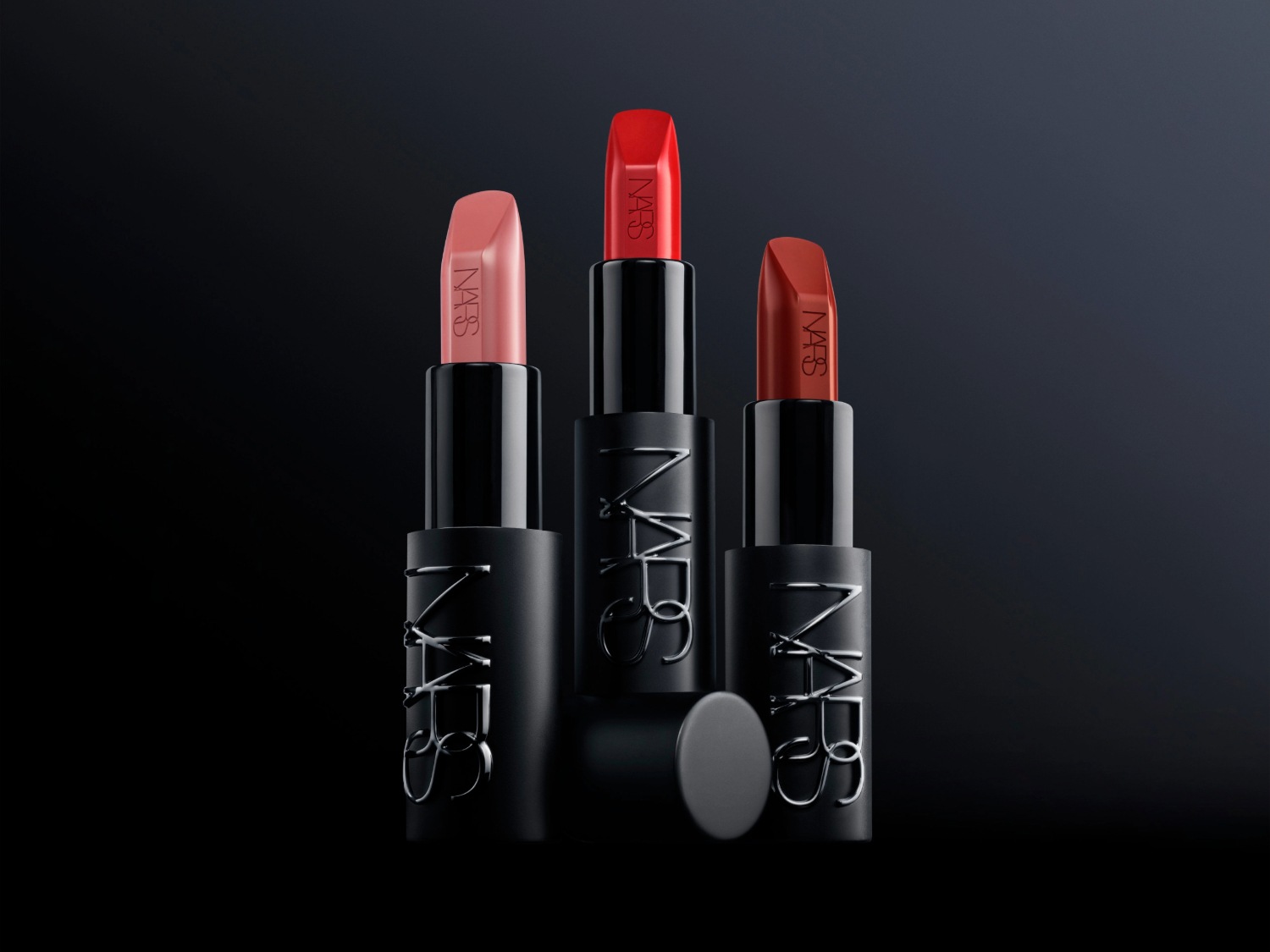 Drie NARS-lipsticks in verschillende tinten, van zachtroze tot helderrood, gepresenteerd in elegante, matzwarte hulzen met het iconische NARS-logo.