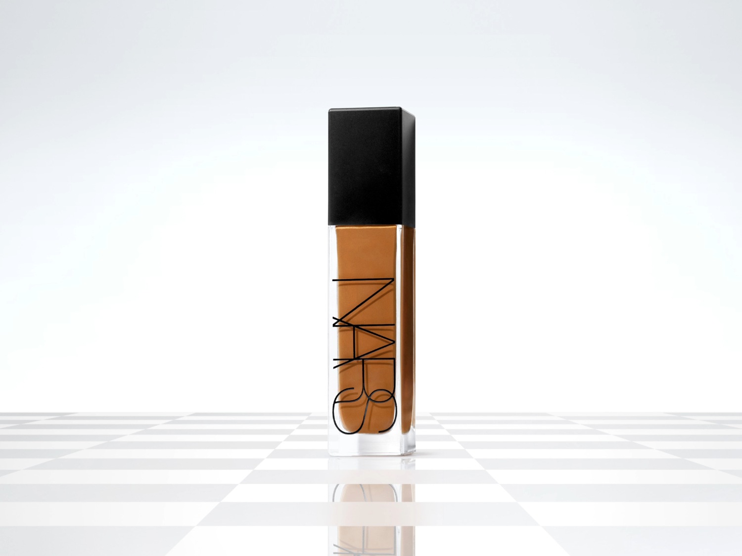 NARS foundation in een heldere glazen fles met een zwarte dop, de vloeistof is bruin.