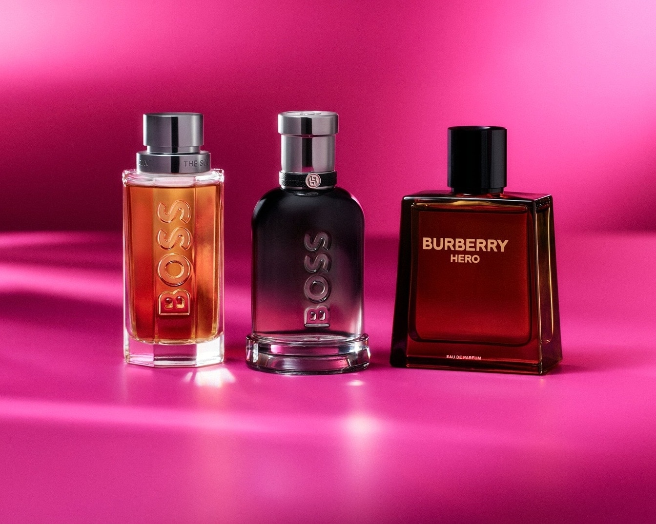 Drei Parfümflaschen von BOSS und Burberry Hero stehen vor einem leuchtend pinkfarbenen Hintergrund.
