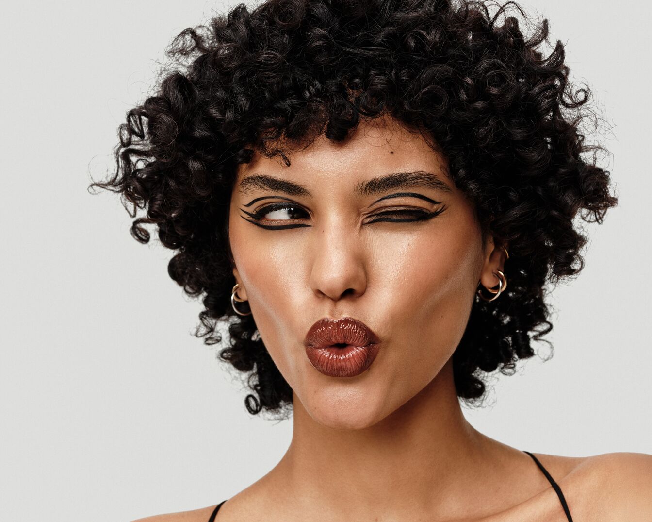 A göndör hajú, barna bőrű nő fekete tusvonallal és fényes, barna ajkakkal kokettál.
