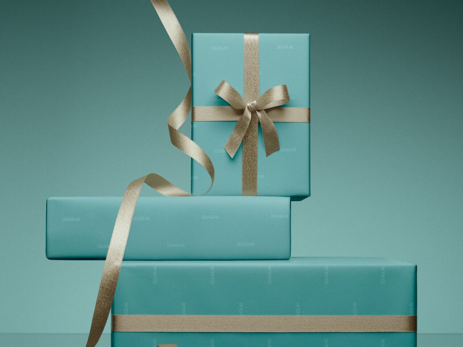Trys dovanų dėžutės, suvyniotos į turkio spalvos popierių su auksiniais kaspinais, sukrautos viena ant kitos, puikiai tinka dovanoms iš Douglas.