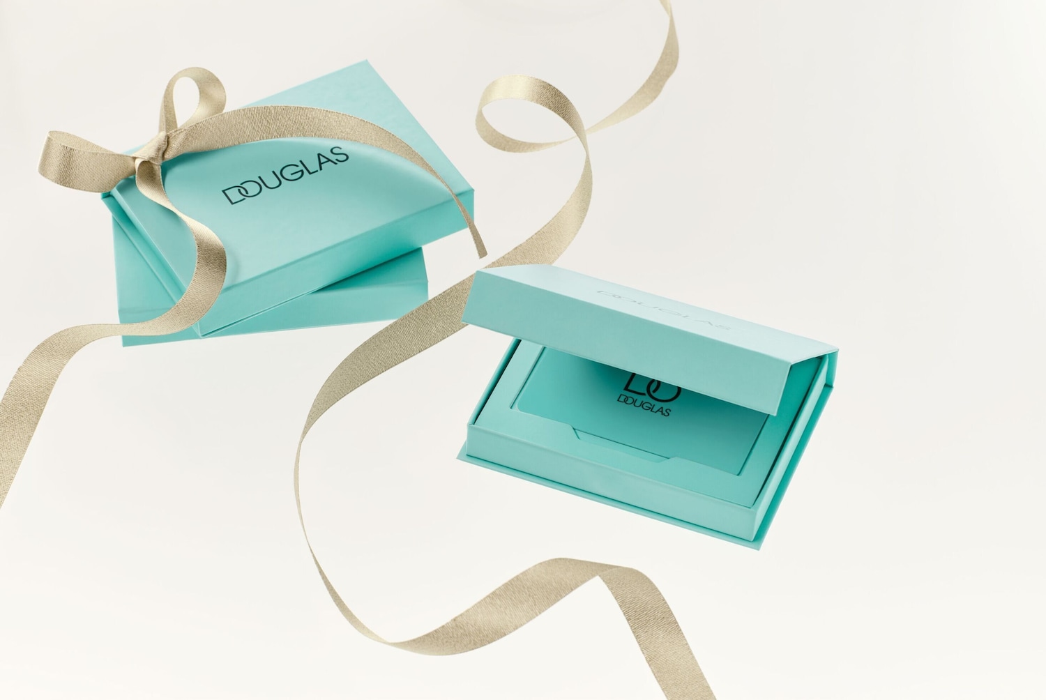 Šviesiai mėlynos spalvos „Douglas“ dovanų dėžutės, papuoštos auksiniu kaspinu, suteikia prabangos ir elegancijos įspūdį.