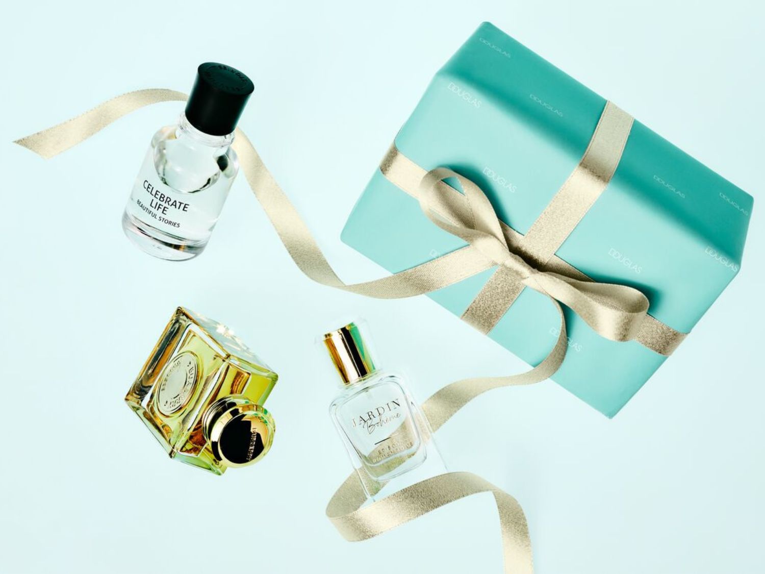 Három parfümös üveg látható, köztük a Celebrate Life és a Jardin Bohème, valamint egy türkizkék Douglas ajándékdoboz arany szalaggal átkötve.