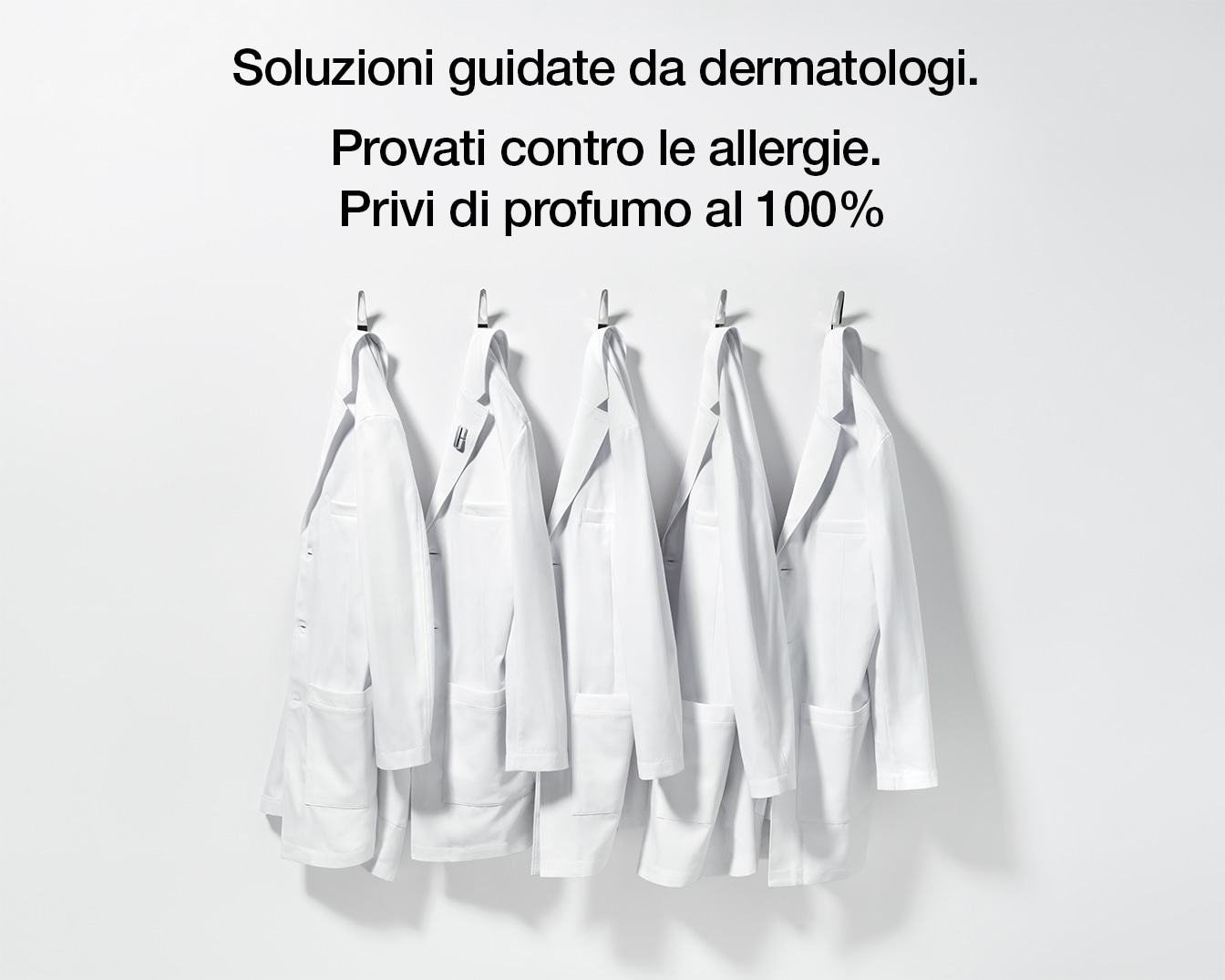 Five white lab coats hang on hooks against a white wall, symbolizing dermatologist-guided, allergy-tested, and 100% fragrance-free solutions.