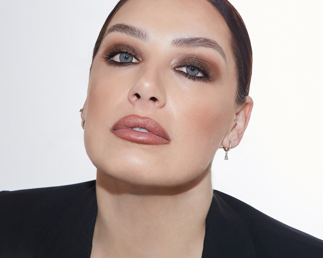 Primo piano di una donna con ombretto marrone scintillante, labbra color carne e blazer nero, che mostra un look sofisticato e moderno.