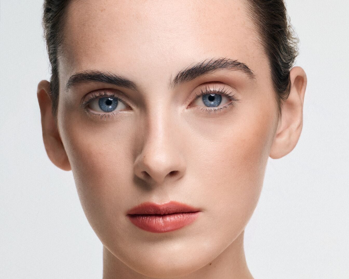 Nahaufnahme eines Frauengesichts mit strahlend blauen Augen, zarten Lippen in einem sanften Korallton und natürlich geformten Augenbrauen.