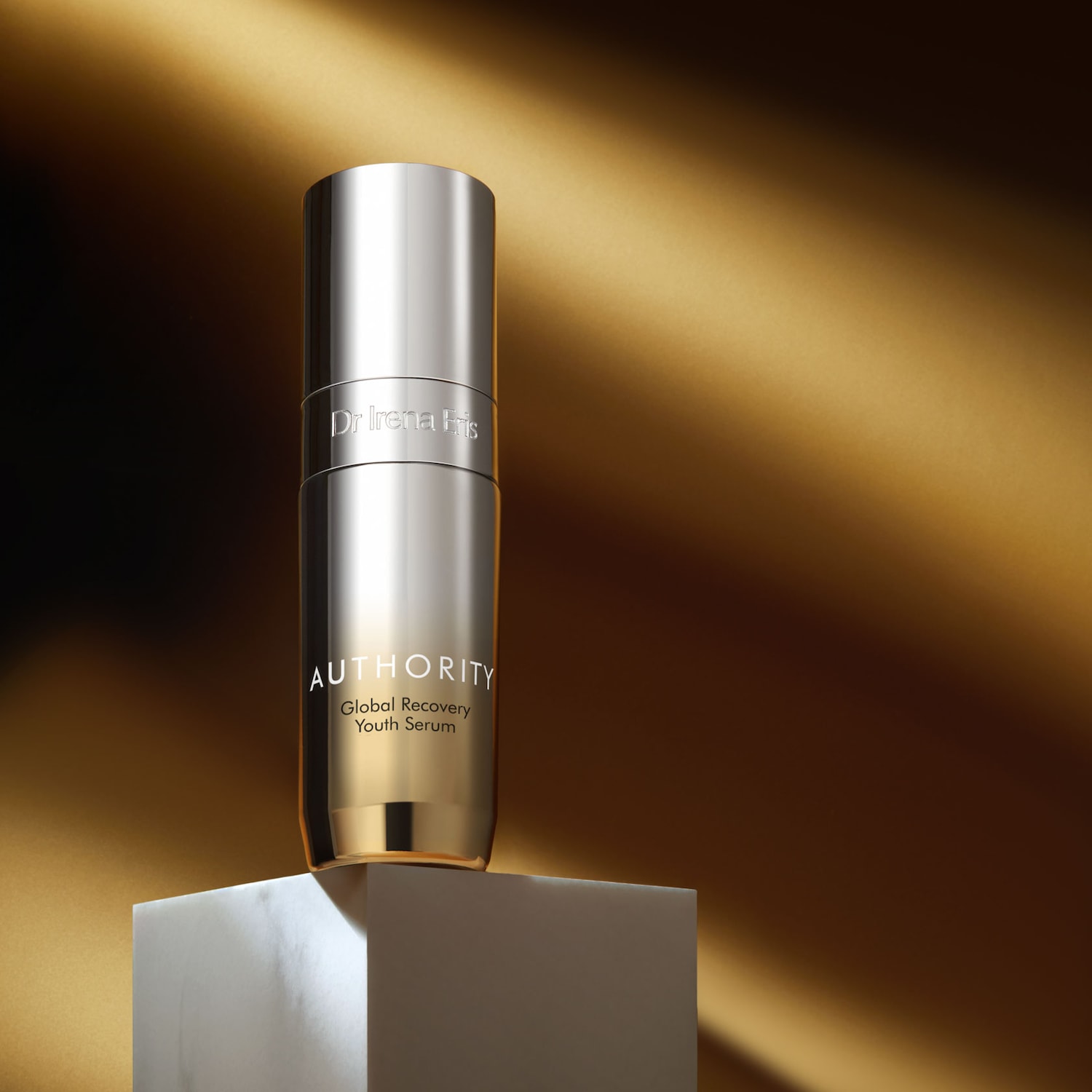 Butelka serum do twarzy Dr Irena Eris Authority Global Recovery Youth Serum w srebrnym opakowaniu na białym postumencie.