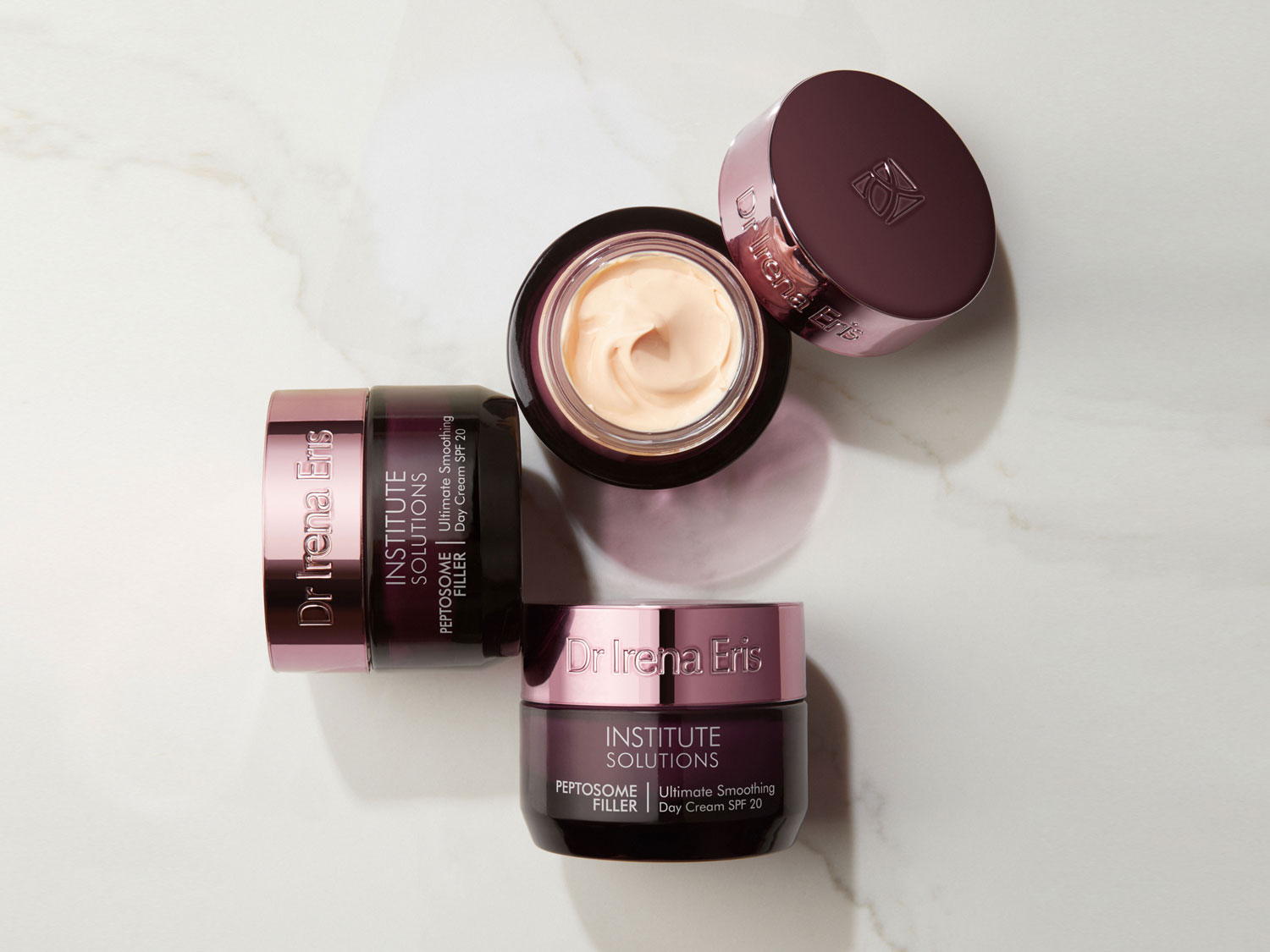 Krem do twarzy Dr Irena Eris Institute Solutions Peptosome Filler Ultimate Smoothing Day Cream SPF 20 w ciemnofioletowym słoiczku z różową nakrętką, obok otwarty słoiczek z kremową zawartością.