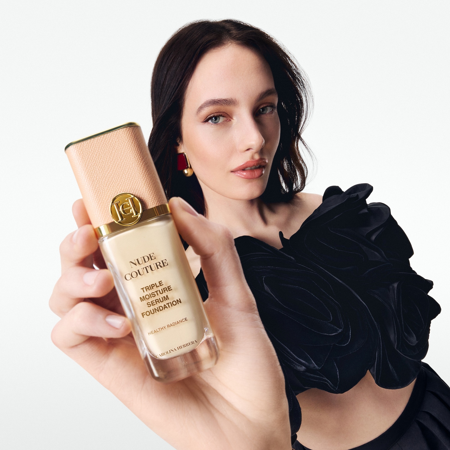Eine Frau hält Carolina Herrera Nude Couture Triple Moisture Serum Foundation mit beigem Deckel und goldenem Logo in der Hand.