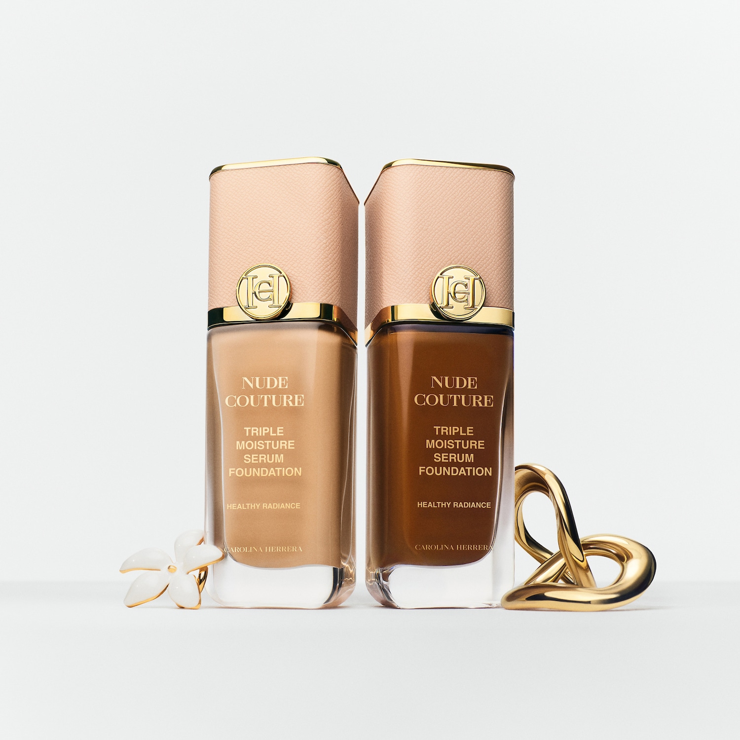 Zwei Flaschen Carolina Herrera Nude Couture Triple Moisture Serum Foundation, eine in hellem und eine in dunklem Farbton, stehen vor einem weißen Hintergrund, der gesunde Glanz verspricht.