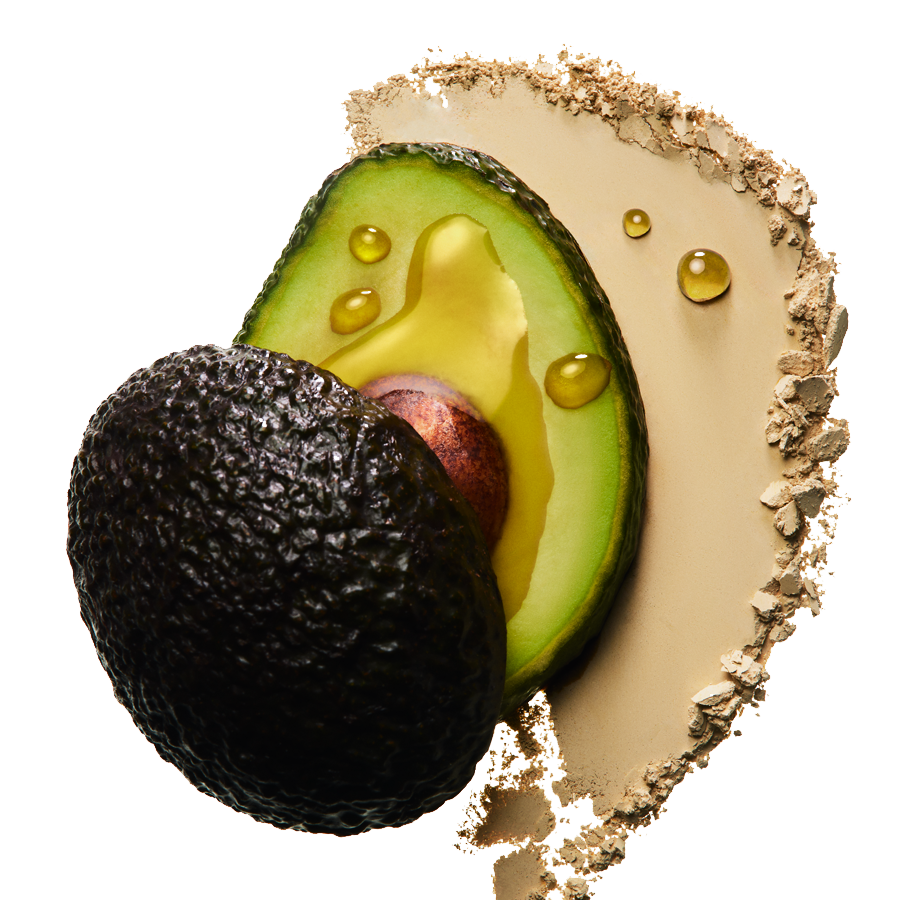 Eine halbe Avocado mit Kern liegt neben einem Haufen beigefarbenem Puder, auf dem ein paar Öltropfen liegen.