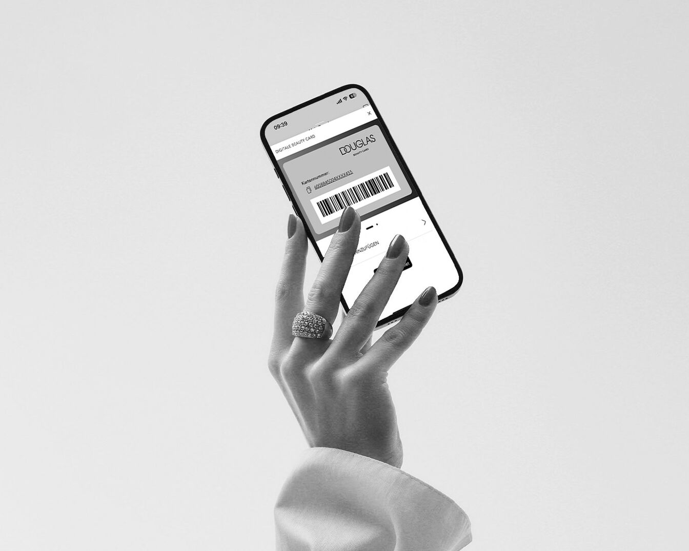 Una mano elegante sostiene un teléfono mostrando la tarjeta de belleza digital de Douglas, con un anillo brillante en el dedo.