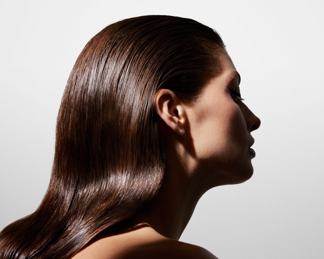 Profilból látható nő, akinek sötétbarna, fényesre lakkozott haja van, ami hátrafelé van fésülve, és a vállára omlik.