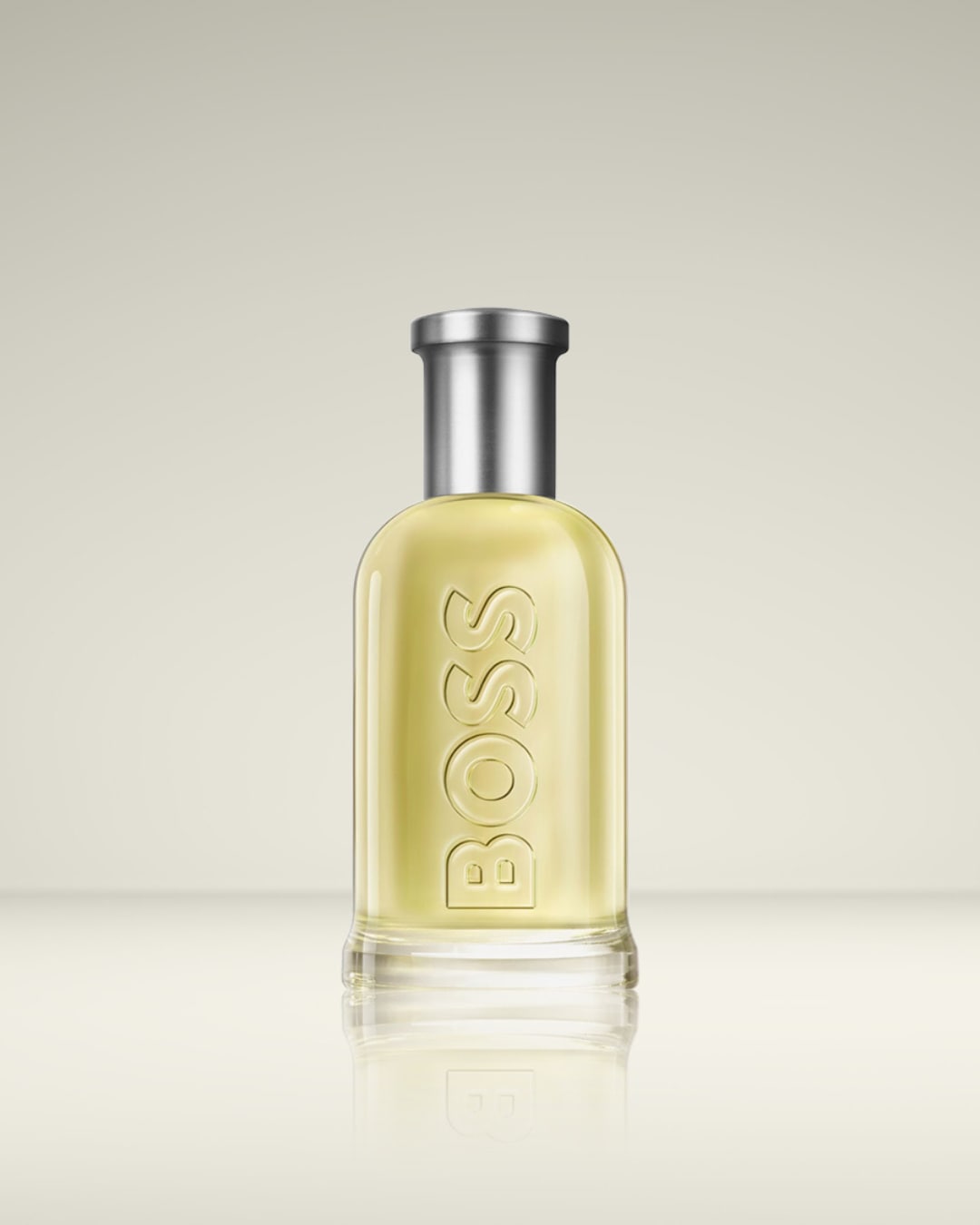 Le parfum BOSS Bottled Eau de Toilette est présenté dans un flacon en verre transparent avec un liquide jaune pâle et un bouchon argenté, le nom "BOSS" est gravé verticalement sur le flacon.