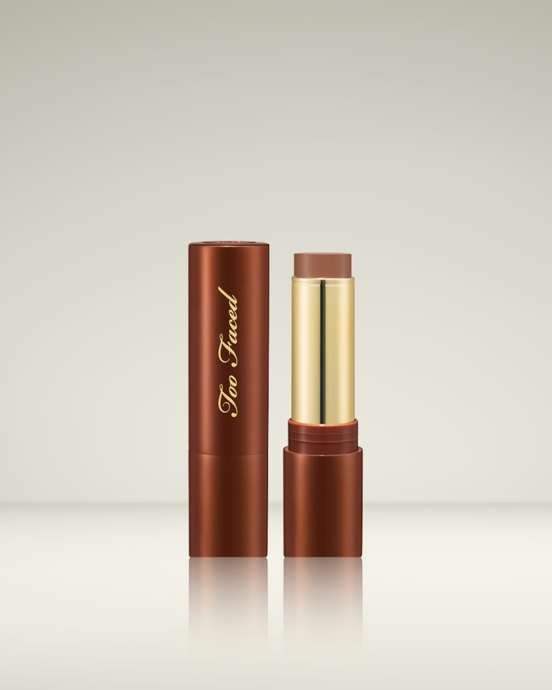 Le stick de fond de teint Too Faced Born This Way en teinte marron est présenté ouvert, révélant le produit de maquillage crémeux et un tube doré, avec le logo de la marque en lettres dorées sur le capuchon.