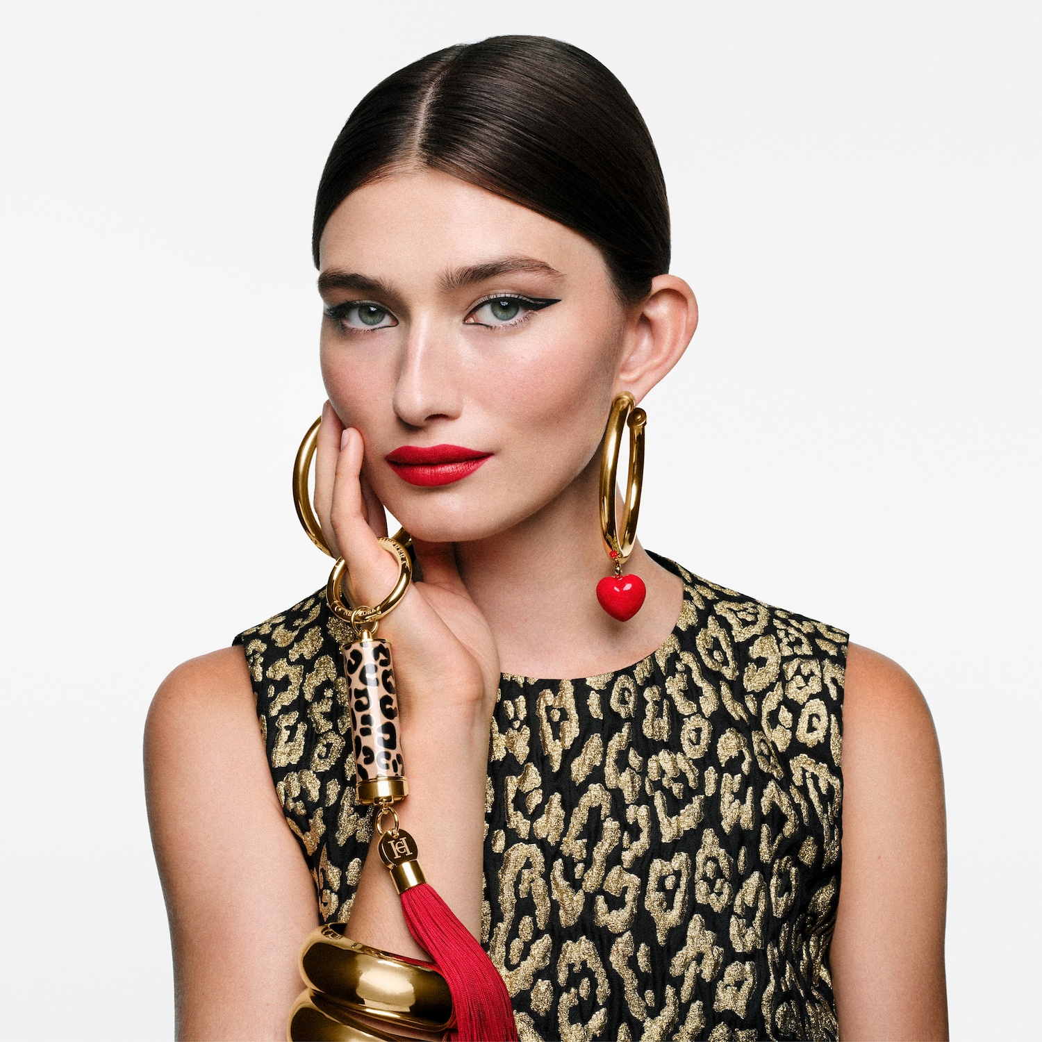 Eine Frau mit roten Lippen, goldenen Ohrringen und einem schwarz-goldenen Kleid mit Leopardenmuster, die einen Schlüsselanhänger mit roter Quaste hält.