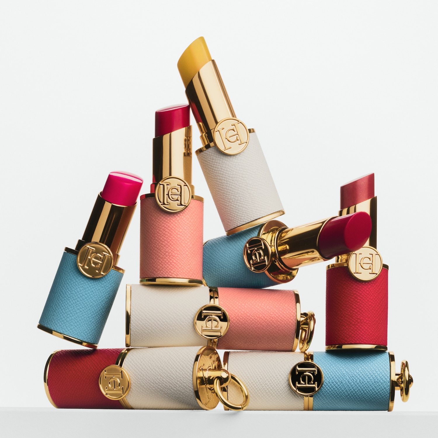 Ein Stapel Carolina Herrera Lippenstifte in verschiedenen Farben und Texturen, von leuchtendem Gelb bis tiefem Rot, alle mit goldenen Akzenten.