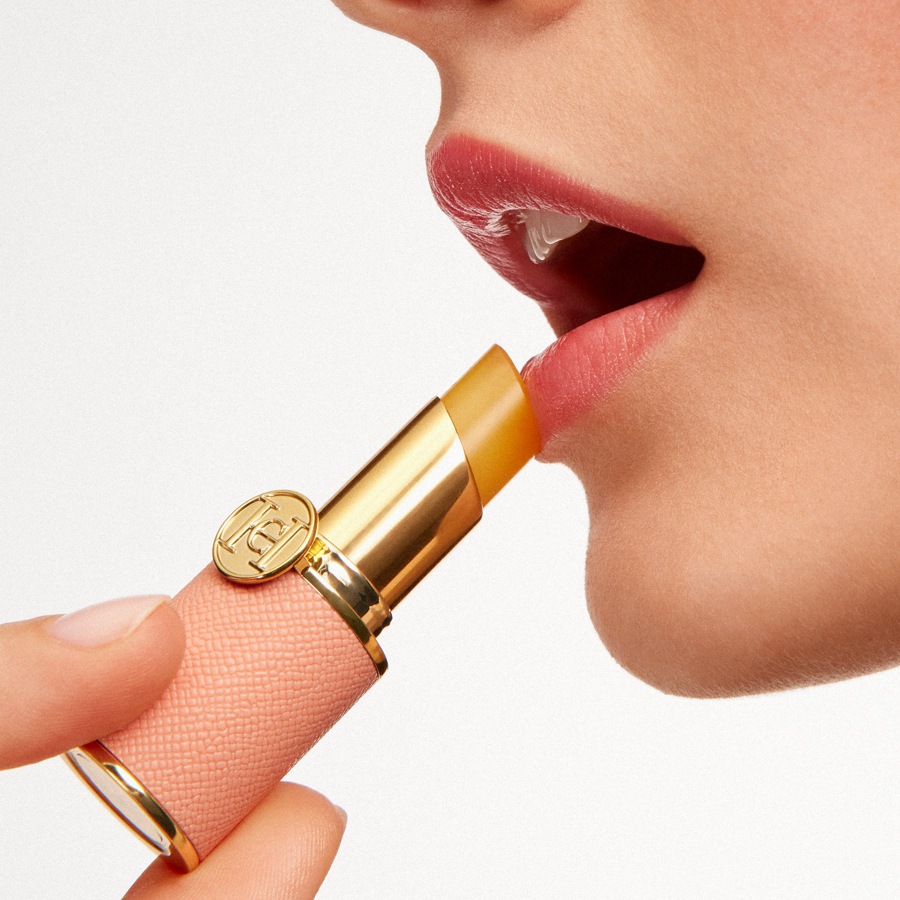 Nahaufnahme einer Frau, die einen gelben Lippenbalsam mit goldener Hülse und rosafarbenem Lederetui aufträgt, um ihre Lippen mit Feuchtigkeit zu versorgen.