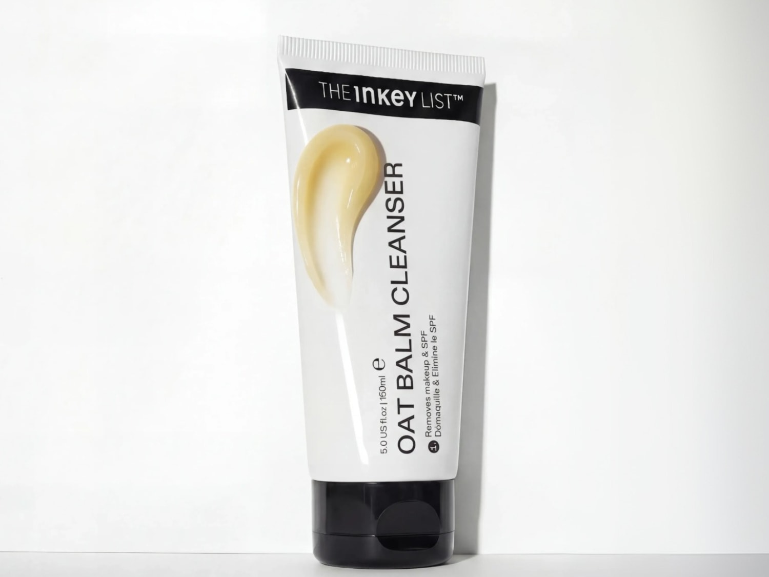 De Inkey List Oat Balm Cleanser in een witte tube met zwarte dop, toont een beige crème die make-up en SPF verwijdert, met een inhoud van 150 ml.