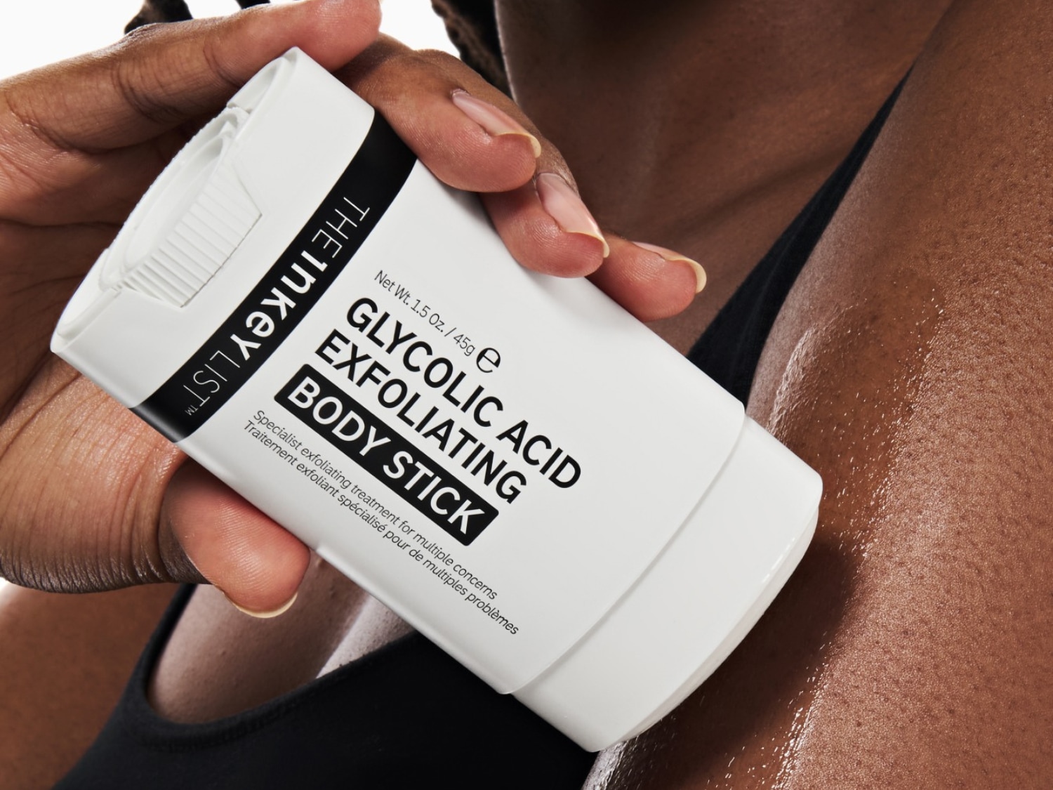 Een hand houdt de witte Glycolic Acid Exfoliating Body Stick van The Inkey List vast, die op een vochtige huid wordt aangebracht.