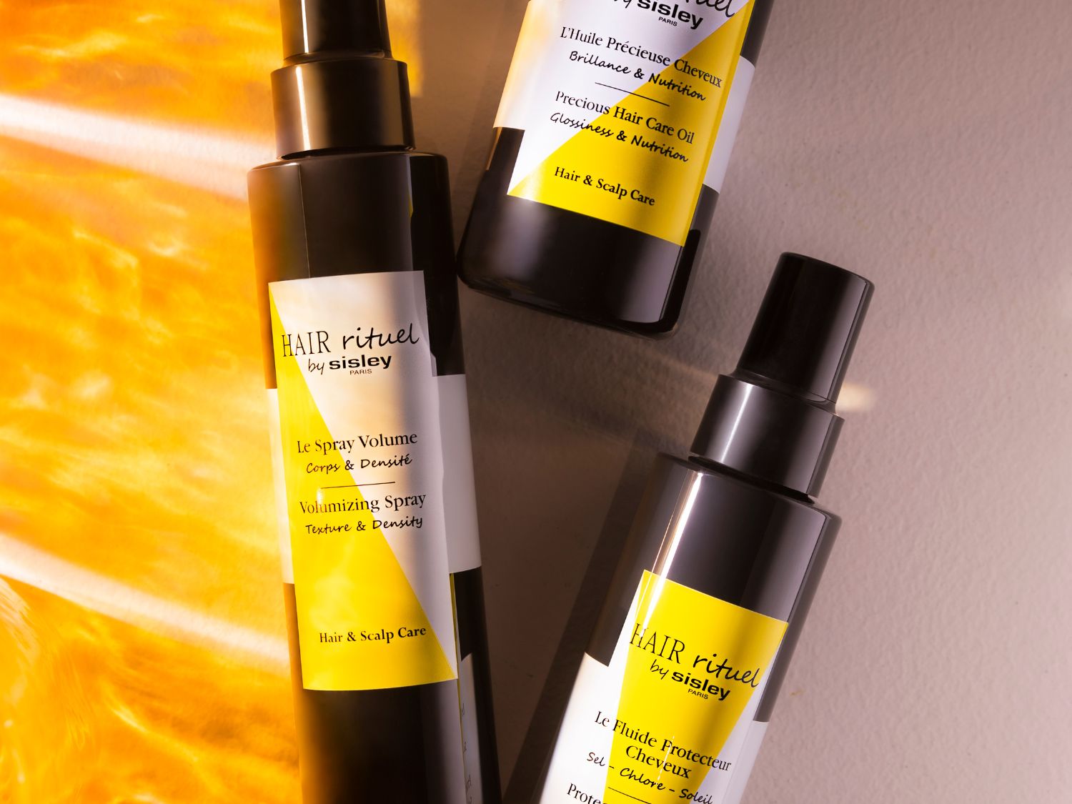 Drie zwarte flessen Hair Rituel by Sisley Paris, waaronder Le Spray Volume voor textuur en dichtheid, en L'Huile Précieuse Cheveux voor glans en voeding.