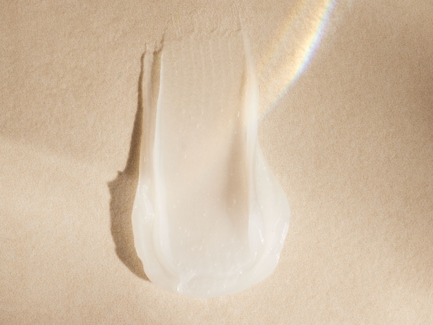 Nahaufnahme eines Klecks einer weißen, leicht transparenten Creme auf beigem Grund, der die Textur und Konsistenz des Produkts zeigt.
