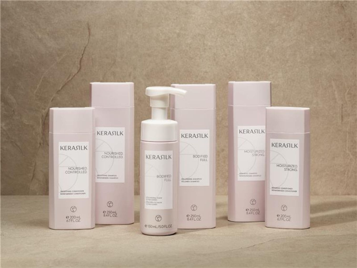 Een reeks KERASILK haarverzorgingsproducten in zachtroze verpakkingen, waaronder shampoo, conditioner en stylingproducten, gepresenteerd op een neutrale achtergrond.