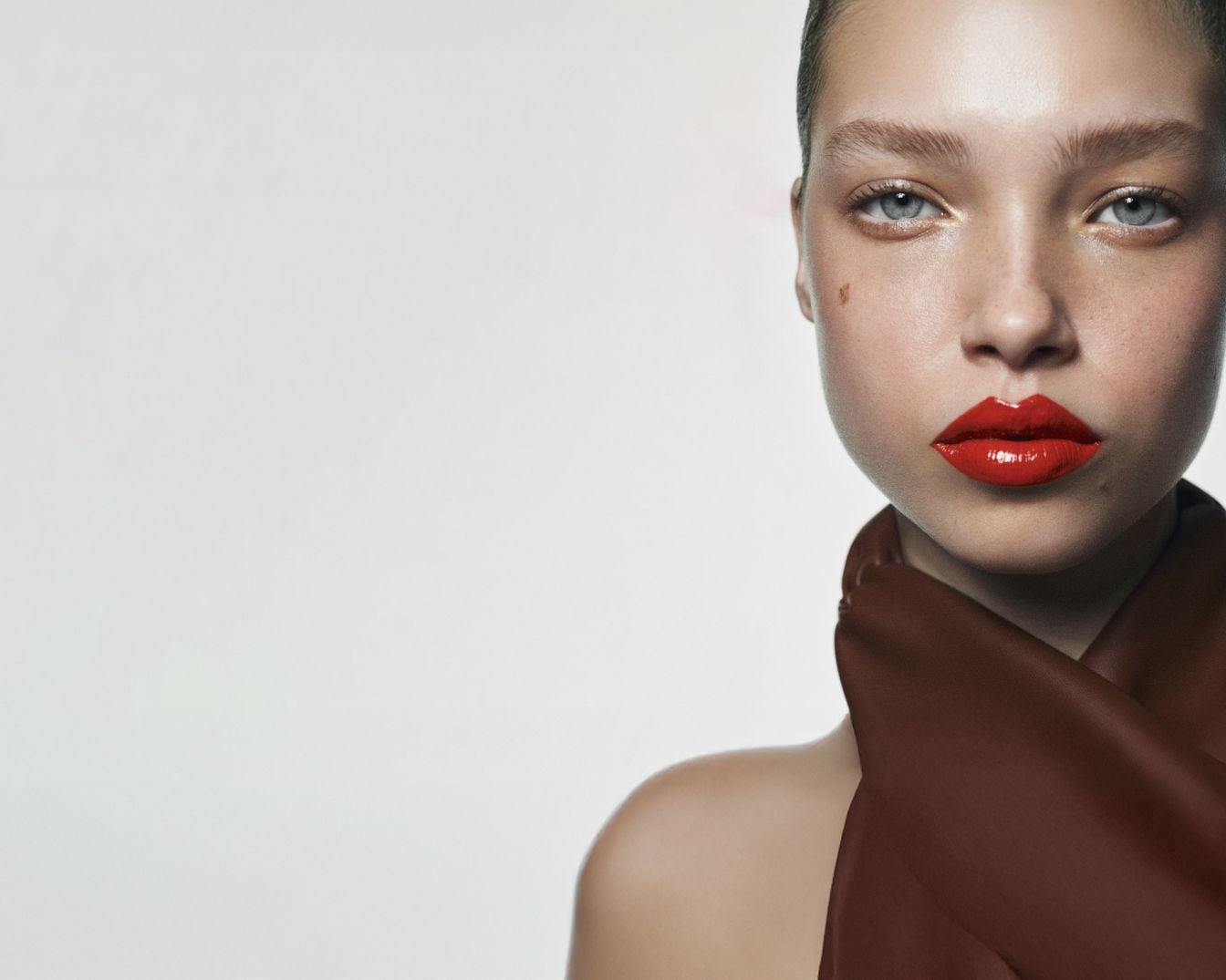 Een close-up van een vrouw met een heldere rode glanzende lippenstift en een bruine doek om haar nek.