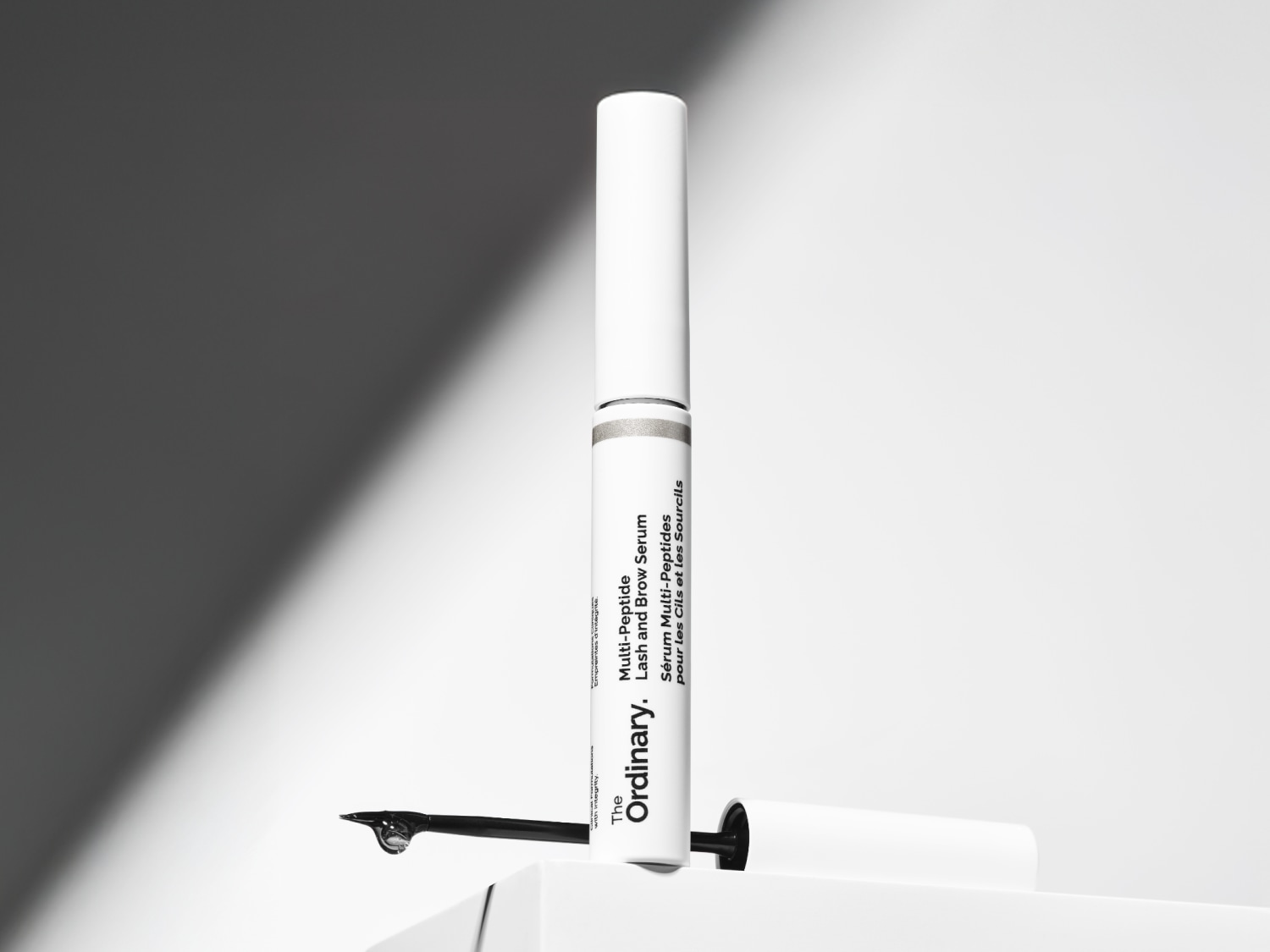 Das Multi-Peptid-Lash- und Brow-Serum von The Ordinary in einer weißen Tube mit silbernen Akzenten, präsentiert mit einem Tropfen Serum an der Bürste.